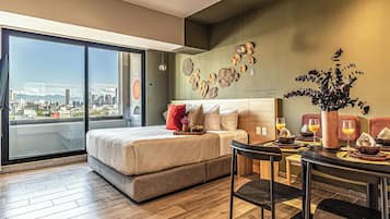 Une chambre d’hôtel moderne avec un grand lit, une table à manger avec des chaises et une vue sur la ville par une grande fenêtre.