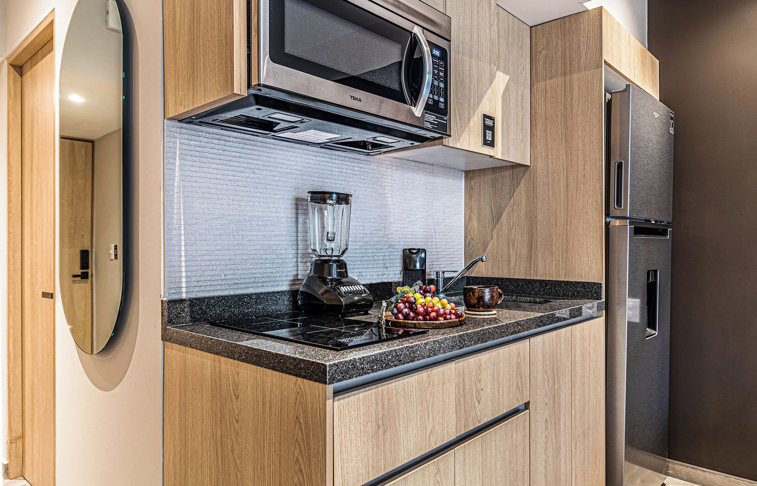 A modern kitchen with a built-in microwave, a blender, and a stainless steel refrigerator.