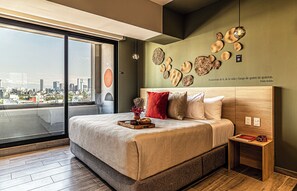 Un dormitorio moderno con vistas a la ciudad, una cama grande, decoración en la pared y una mesita de noche con un libro y una bolsa.