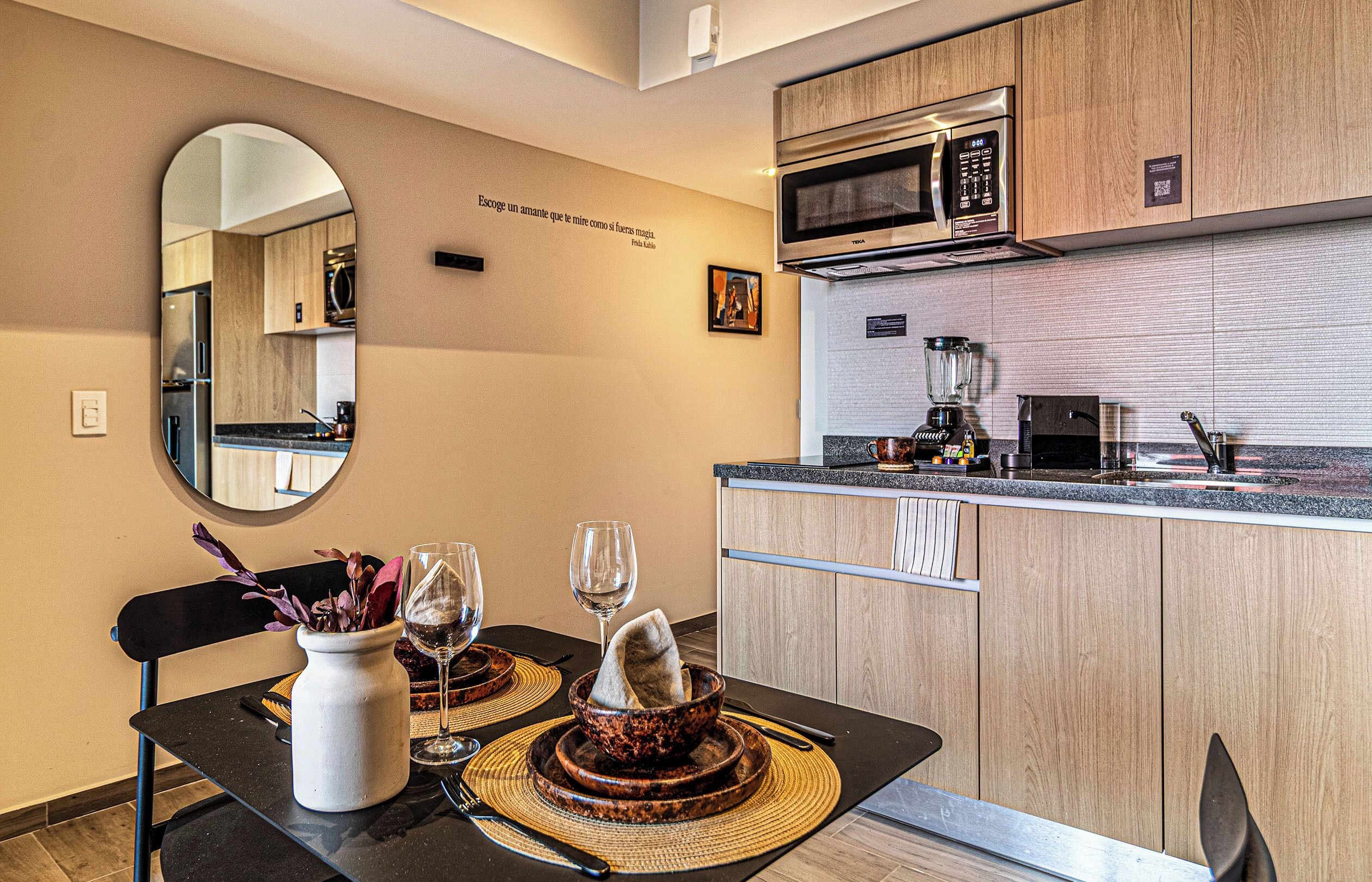 Una cocina moderna con microondas, licuadora y cafetera. Hay una mesa de comedor con un florero y copas de vino.