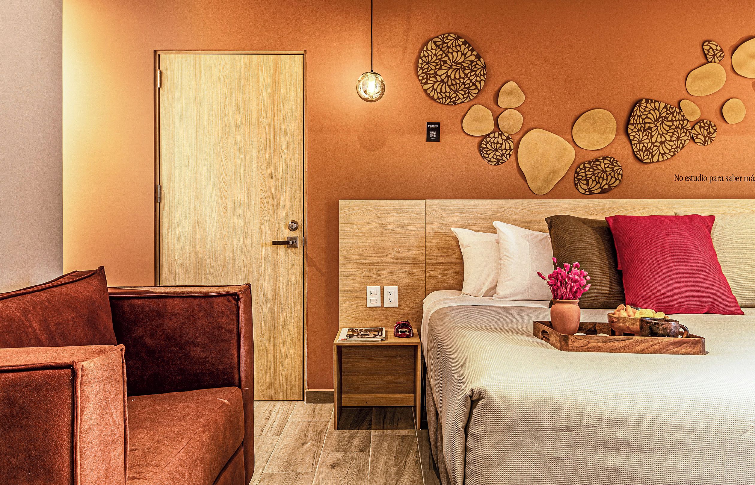 A hotel room with a wooden door, a nightstand with a lamp, a bed with pillows, and a wall decor.