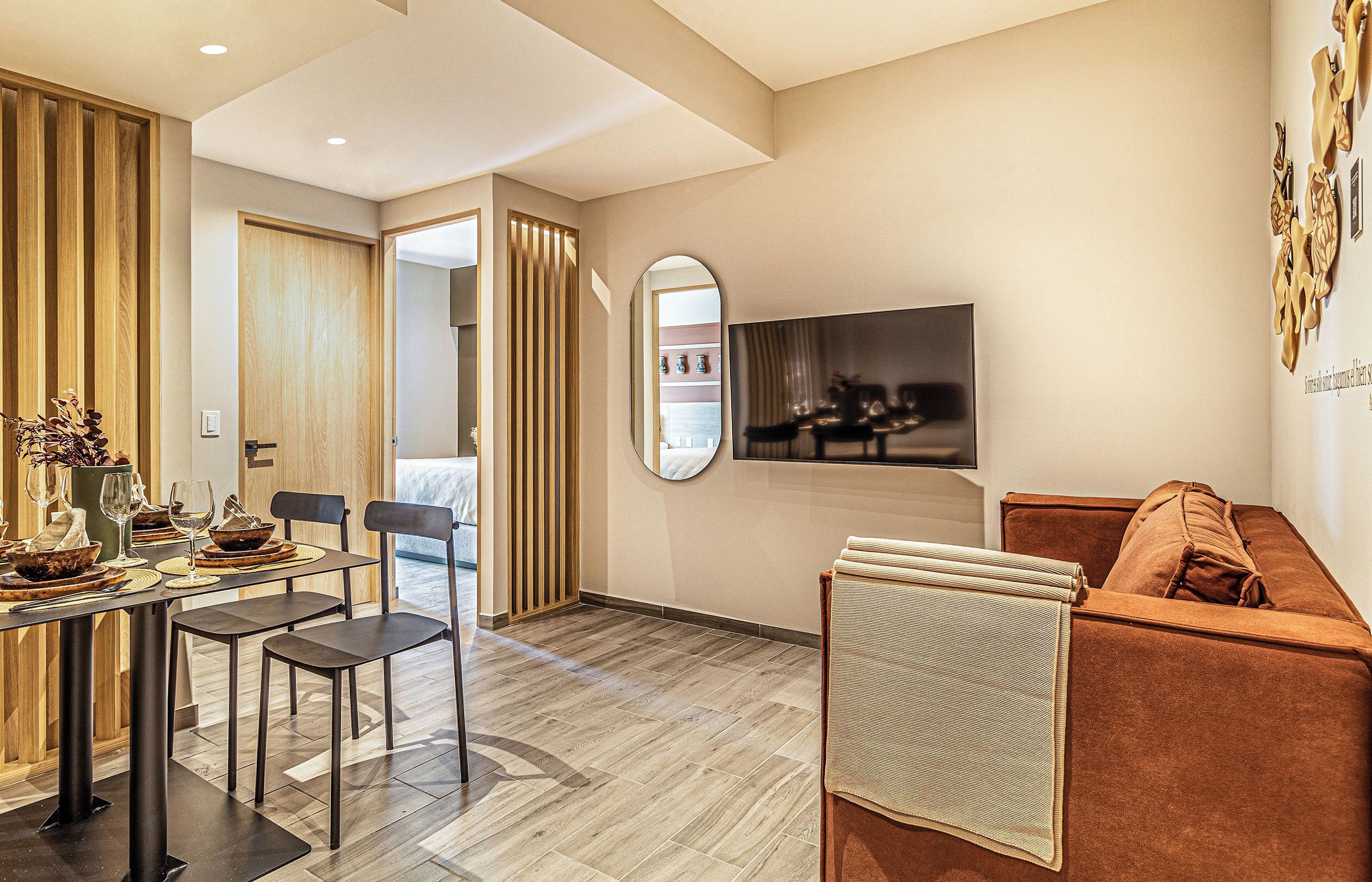 A modern living room with a sofa, a dining area with a table set for two, and a television mounted on the wall.