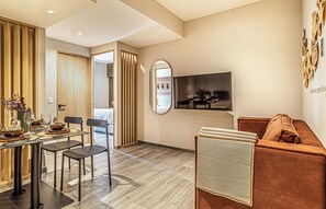 Un salon moderne avec un canapé, un coin repas avec une table dressée pour deux personnes, et un téléviseur fixé au mur.