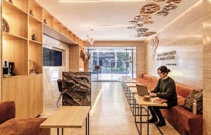 Un interior moderno con estanterías de madera, una pared decorativa de mármol y un área de descanso con mesas y sillas.