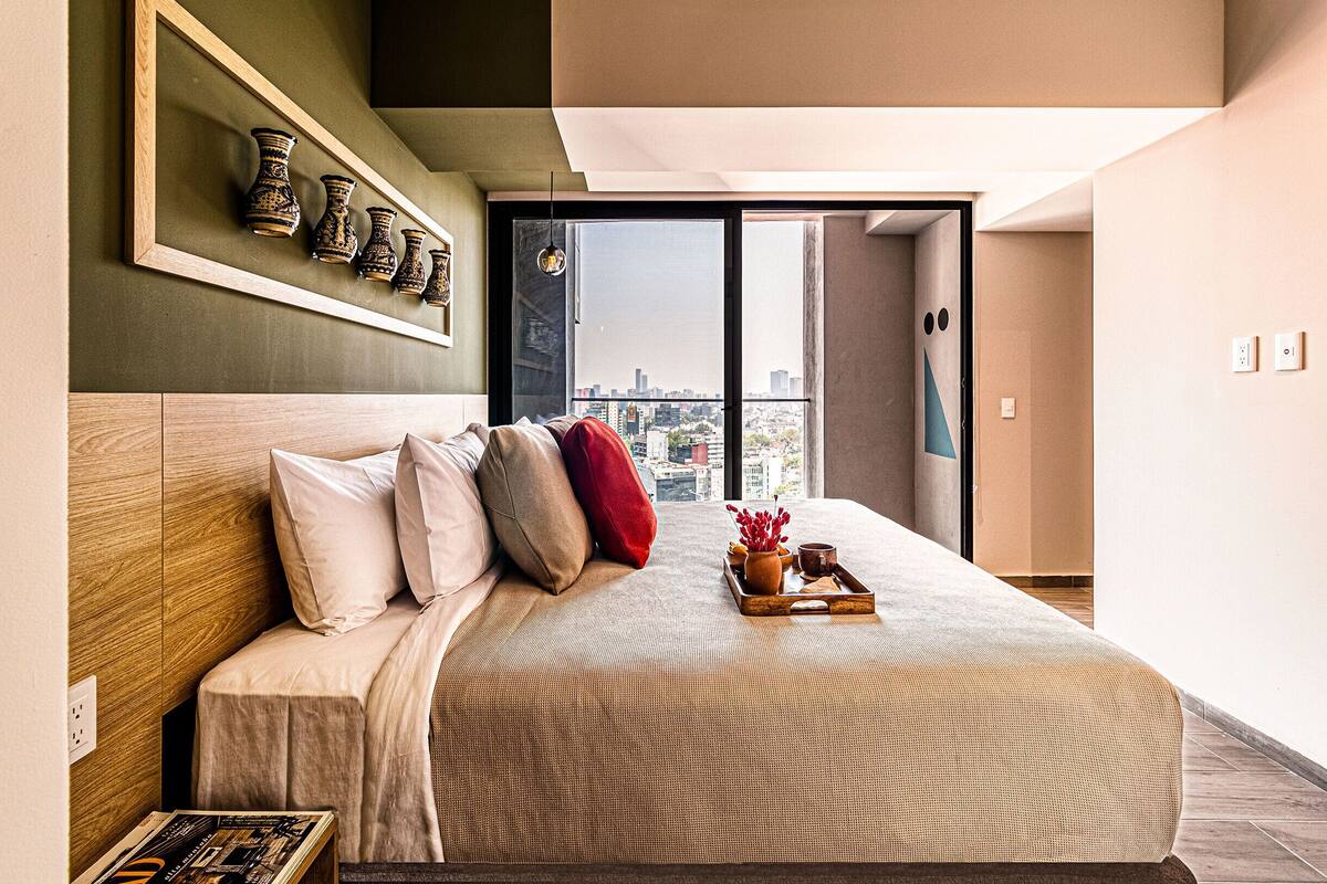 Una habitació d'hotel moderna amb un llit gran, vistes a la ciutat i un capçal de llit de fusta.