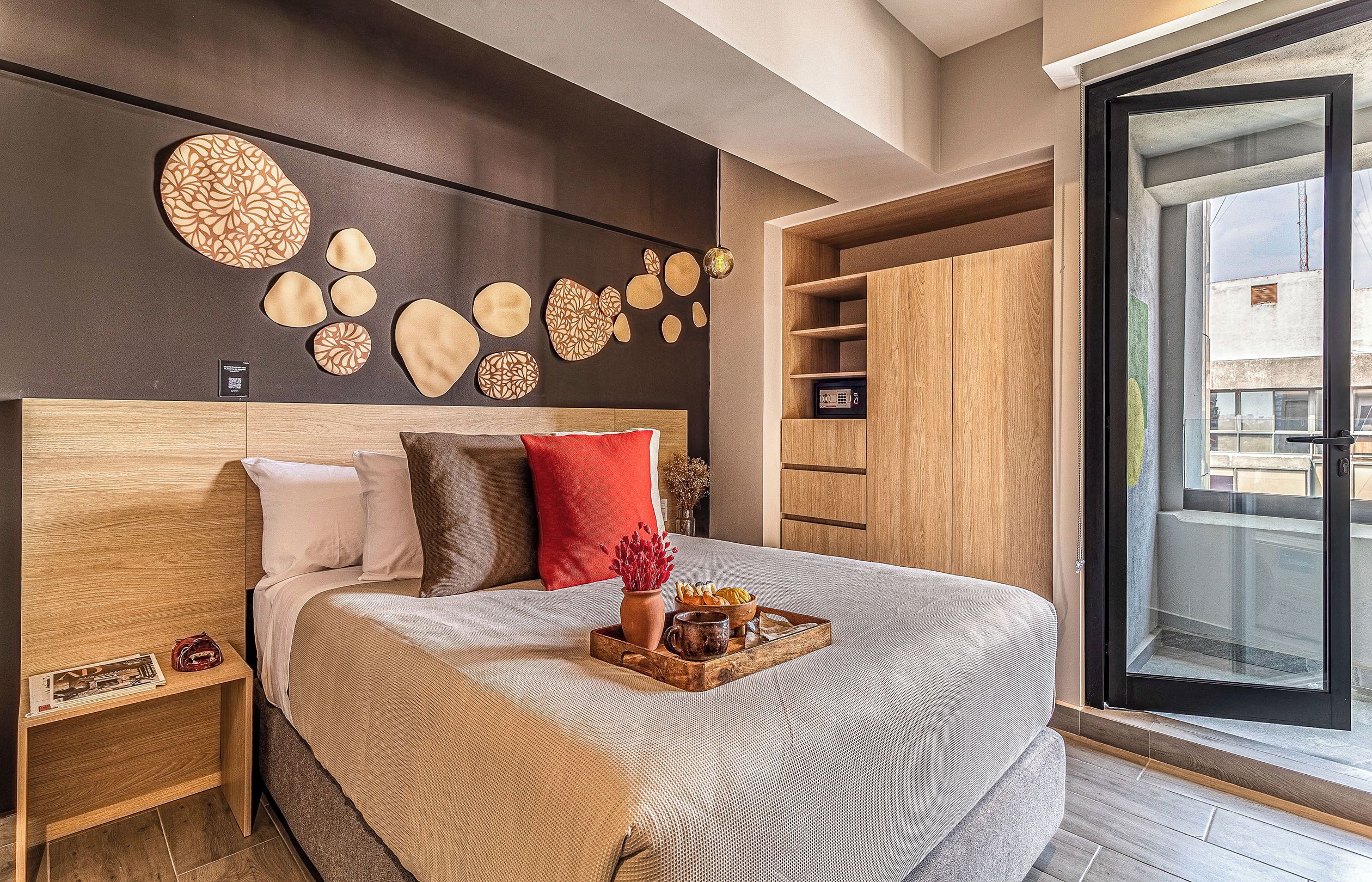 A modern bedroom with a large bed, a wooden headboard, and a view of the city through a large window.