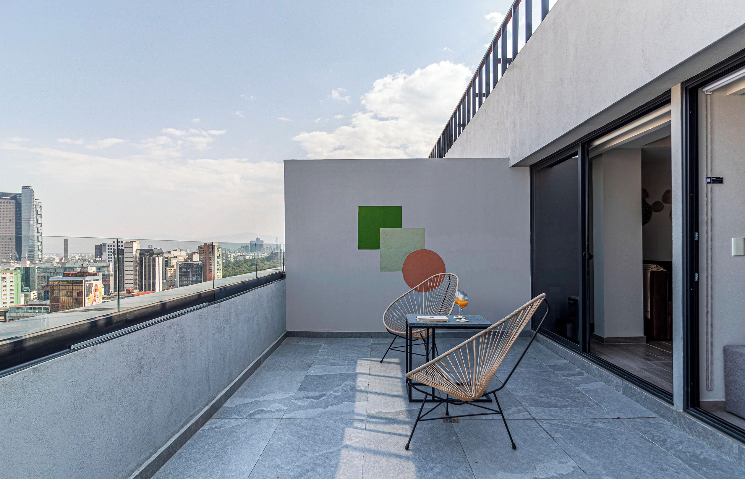 A balcony with a city view, a table with a chair, and a wall with abstract art.