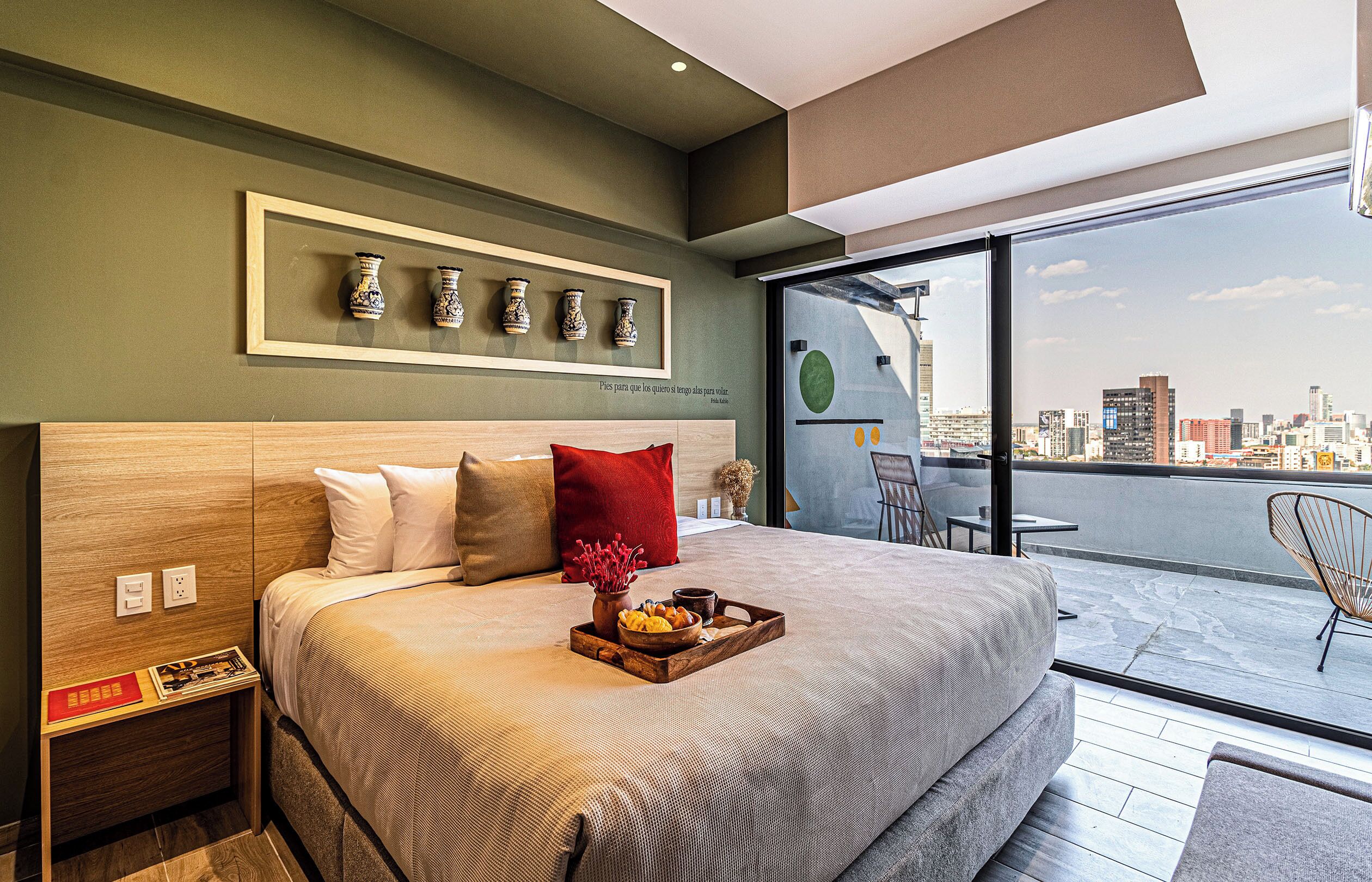 A modern bedroom with a city view, a bed with a wooden headboard, a bedside table, and a tray with snacks.