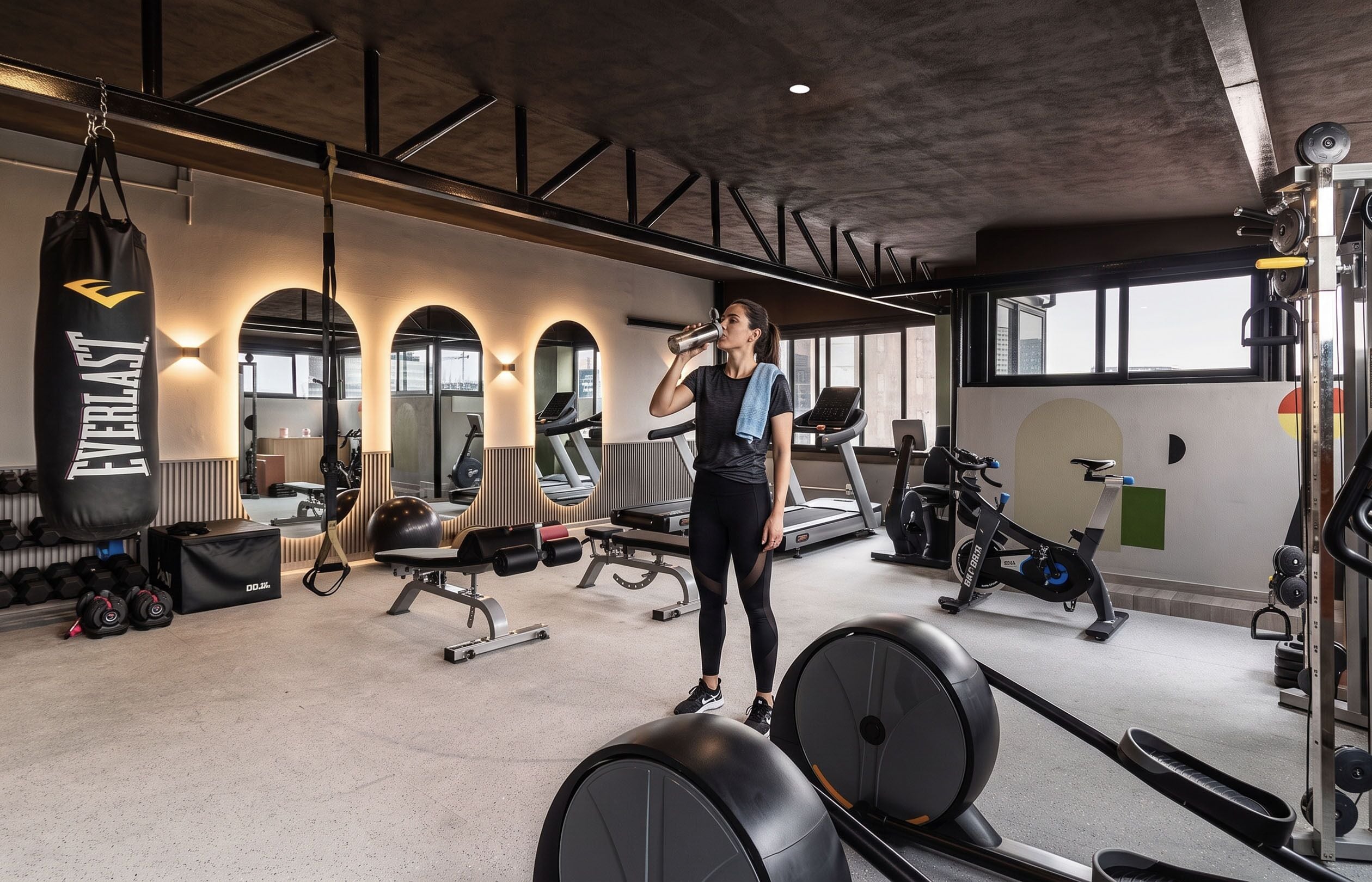 Een sportschool met fitnessapparatuur, een bokszak en een persoon die op een loopband traint.