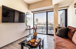 Una sala de estar moderna con una mesa de centro de vidrio, un sofá y vistas a la ciudad a través de amplios ventanales.