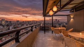 Une terrasse sur le toit offrant une vue sur la ville, avec des sièges en plein air et des guirlandes lumineuses.