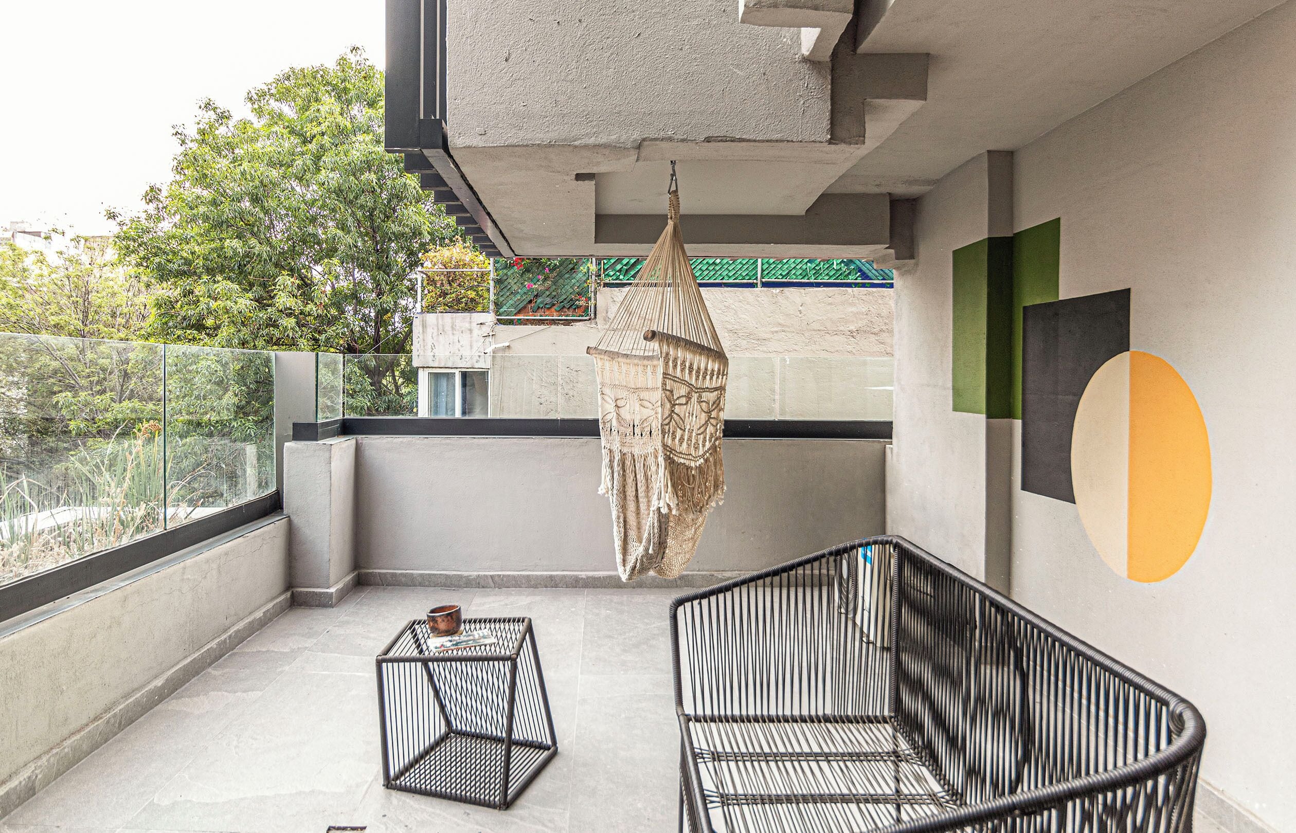 Een balkon met een macramé decoratie, twee metalen stoelen en een tafeltje met een schaal.