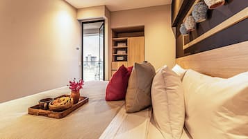 Una habitación de hotel moderna con cama, mesita de madera con bandeja de comida y flores, armario y vistas a la ciudad a través de una ventana.