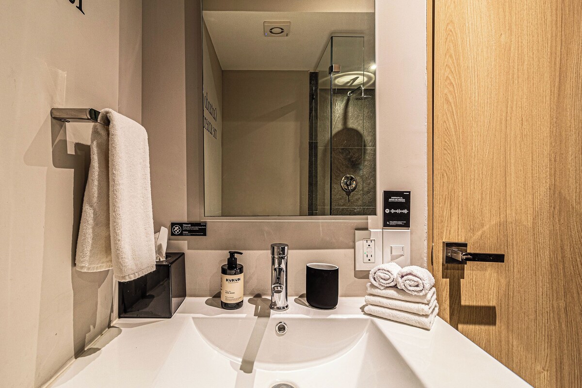 Un baño moderno con lavamanos, espejo, toallero y puerta de madera.