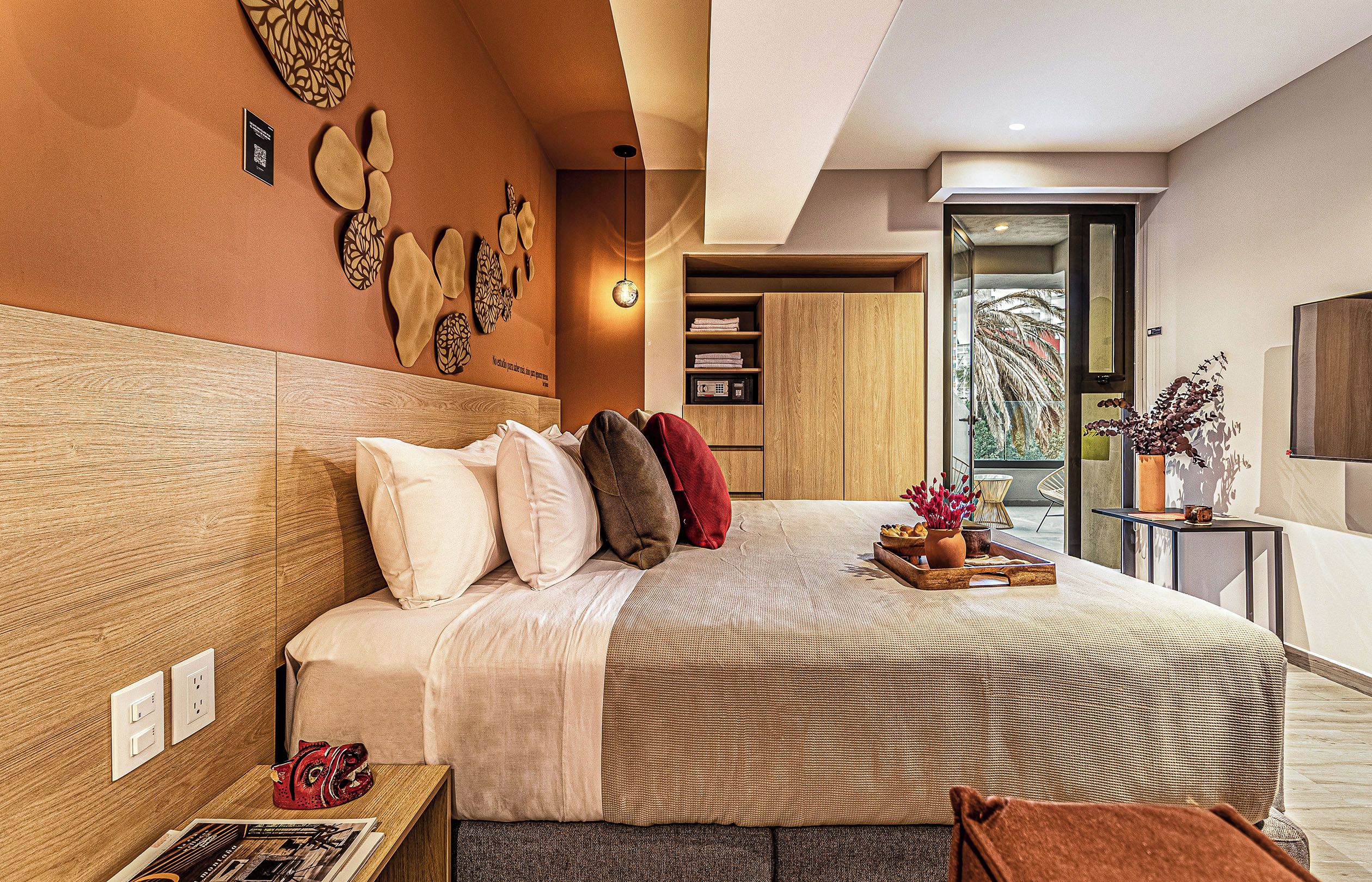 A modern bedroom with a large bed, a wooden headboard, a bedside table with a lamp, and a view of the outdoors through a glass door.
