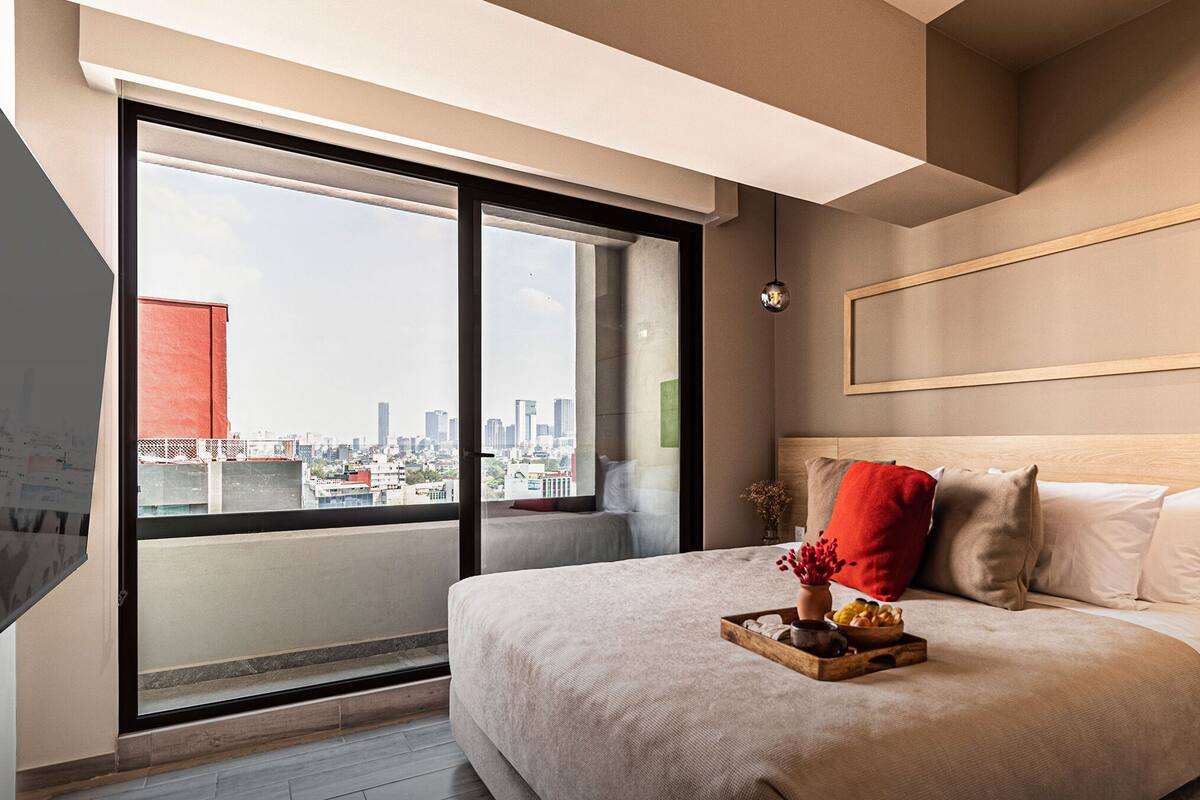 Habitació d'hotel moderna amb un llit gran, vista a la ciutat a través de finestres de fulles mortes i una decoració minimalista.