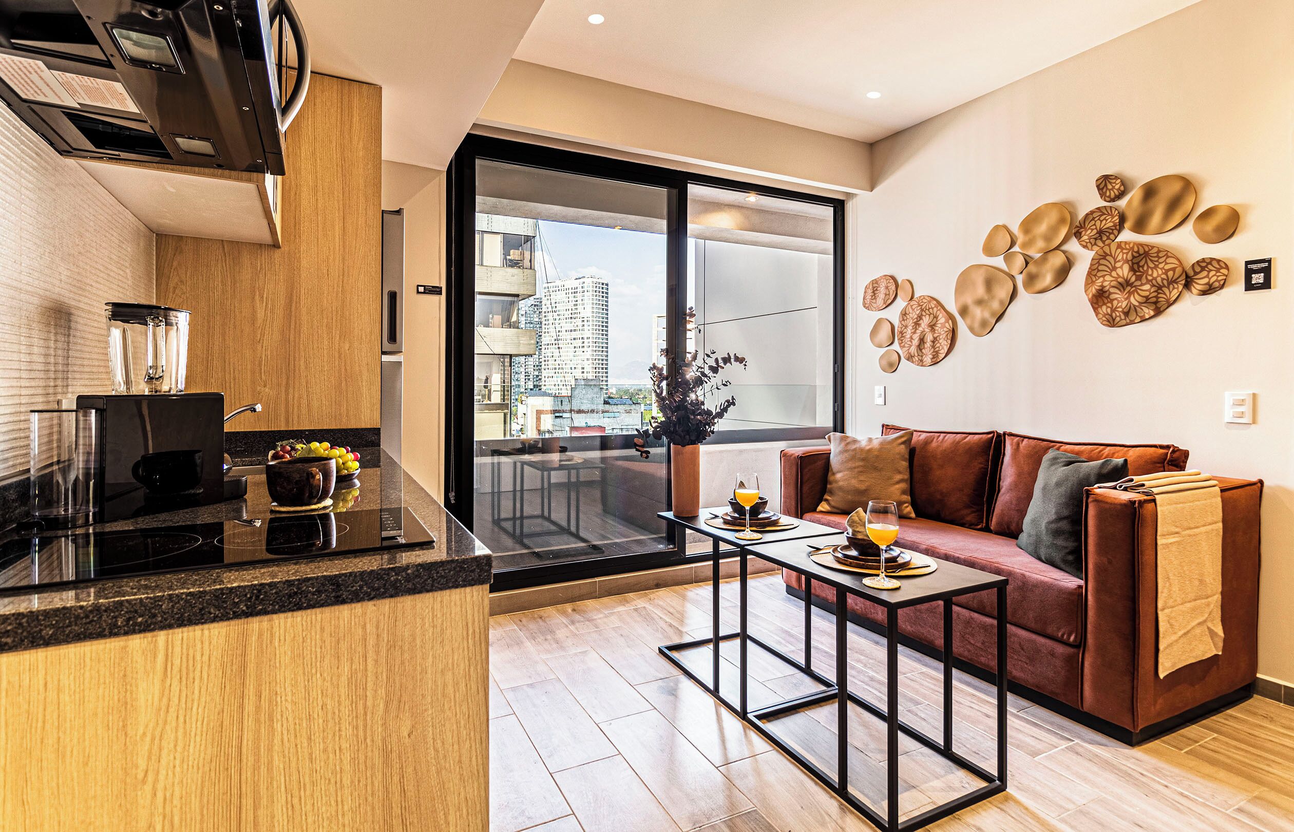 Un apartamento moderno con cocina, comedor y sala de estar con sofá, y un balcón con vistas a la ciudad.