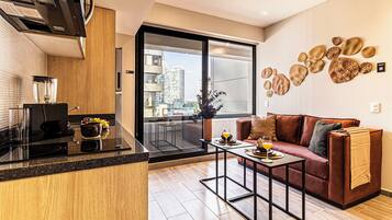 Un apartamento moderno con cocina, comedor y sala de estar con sofá, y un balcón con vistas a la ciudad.