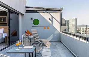 Un balcón moderno con vista a la ciudad, una silla de mimbre, una mesita con bebidas y un libro.