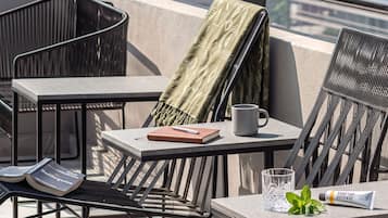 A rooftop terrace with outdoor furniture, a table with a book, a mug, and a tube of sunscreen.