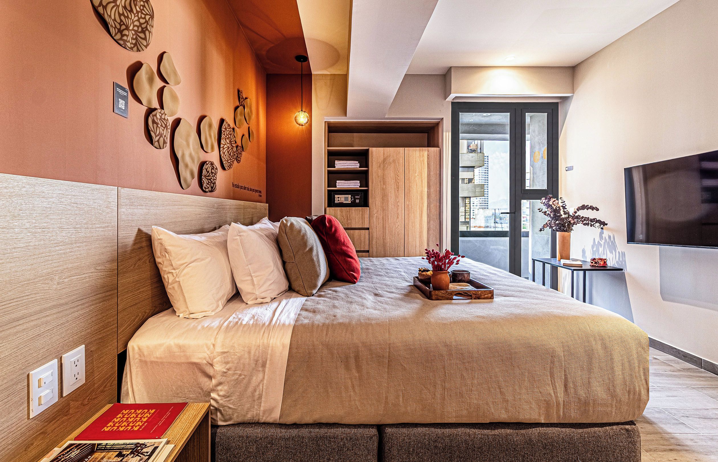 Un dormitorio moderno con una cama grande, un televisor montado en la pared y vistas a la ciudad desde la ventana.