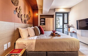 Un dormitorio moderno con una cama grande, un televisor montado en la pared y vistas a la ciudad desde la ventana.