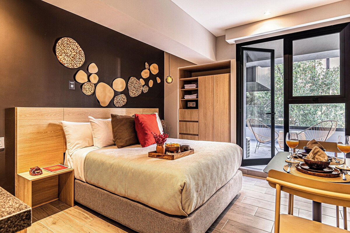Un dormitorio moderno con una cama grande, cabecera de madera, mesita de noche, armario y una obra de arte en la pared, con vistas al exterior a través de un ventanal amplio.