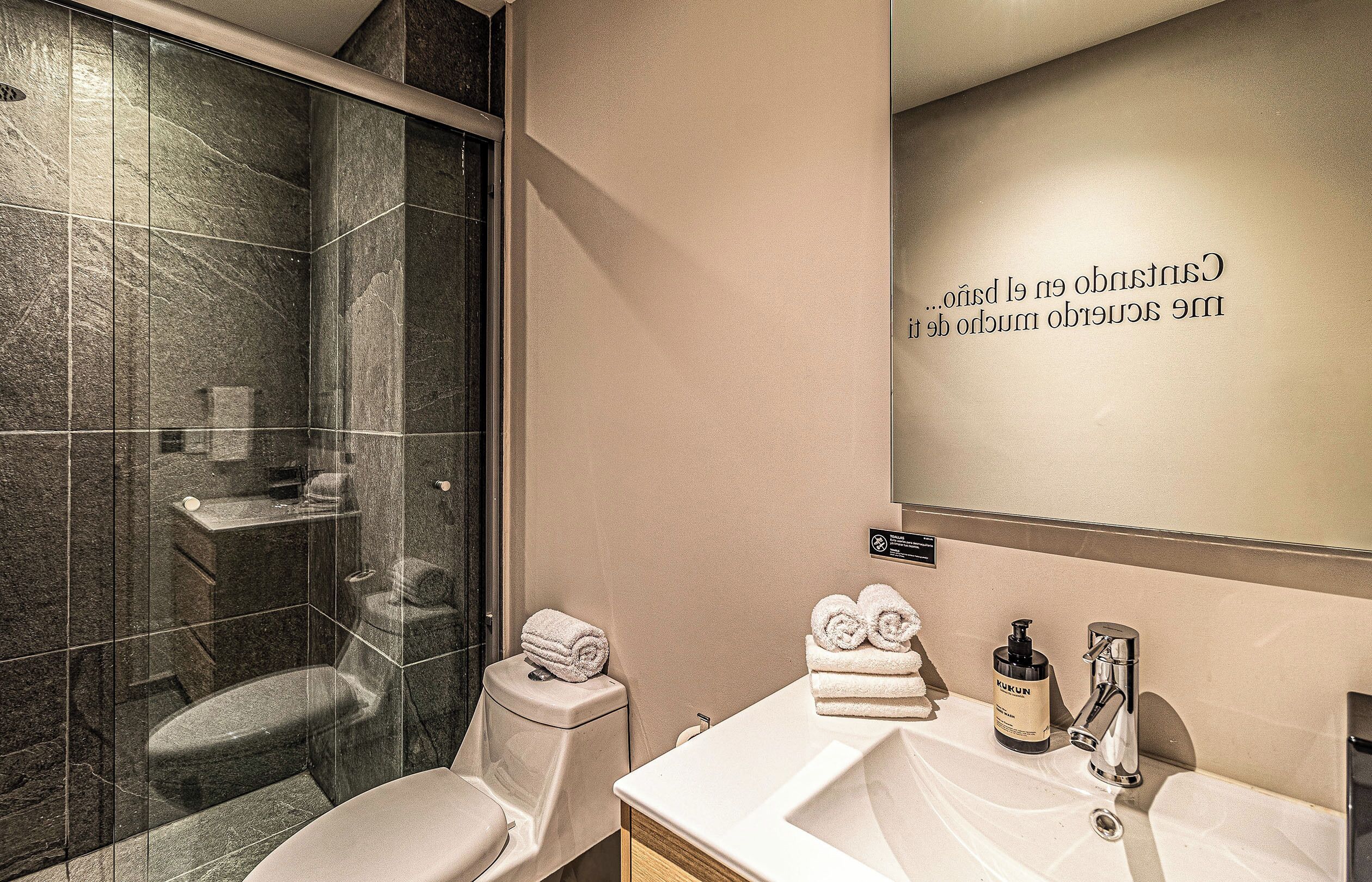 A modern bathroom with a glass-enclosed shower, a toilet, a sink with a mirror, and a towel rack.