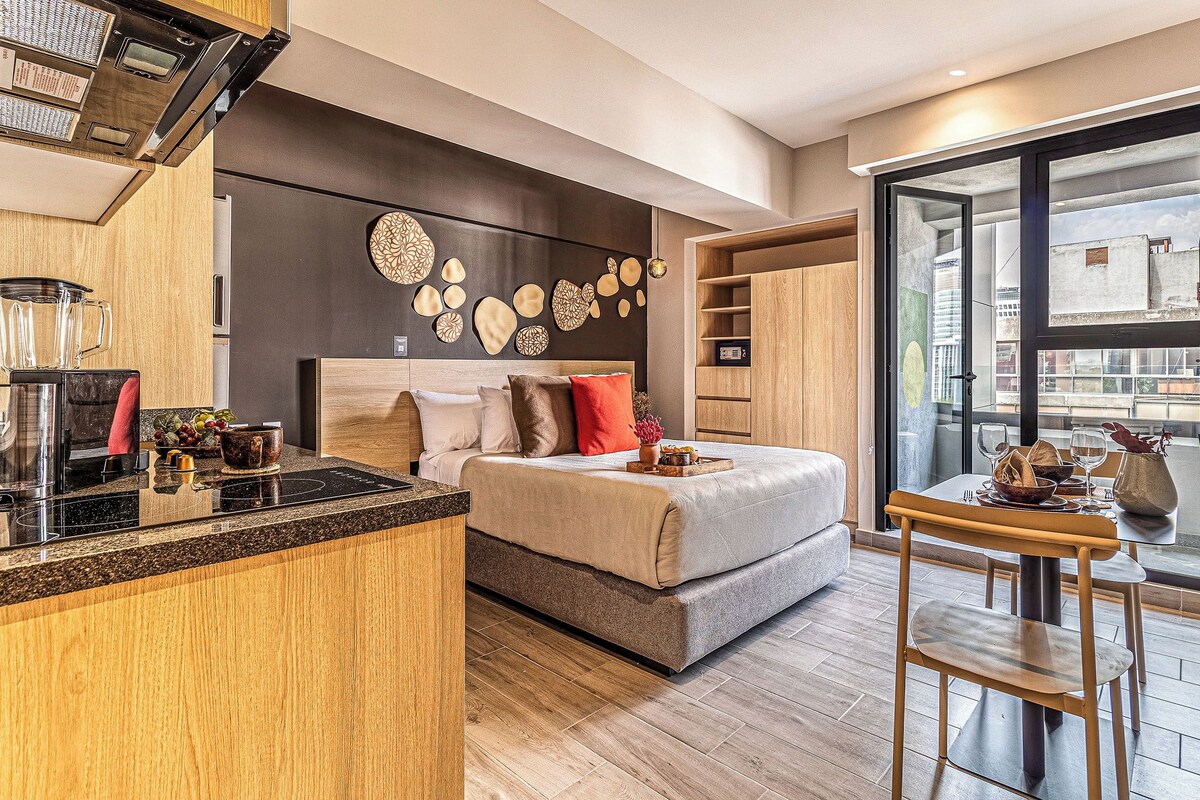 Een moderne slaapkamer met een bed, nachtkastje en een zithoek met een tafel en stoelen.