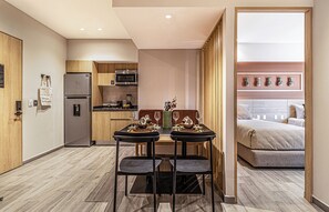 Habitación de hotel compacta con kitchenette, zona de comedor con mesa y sillas, y una cama.