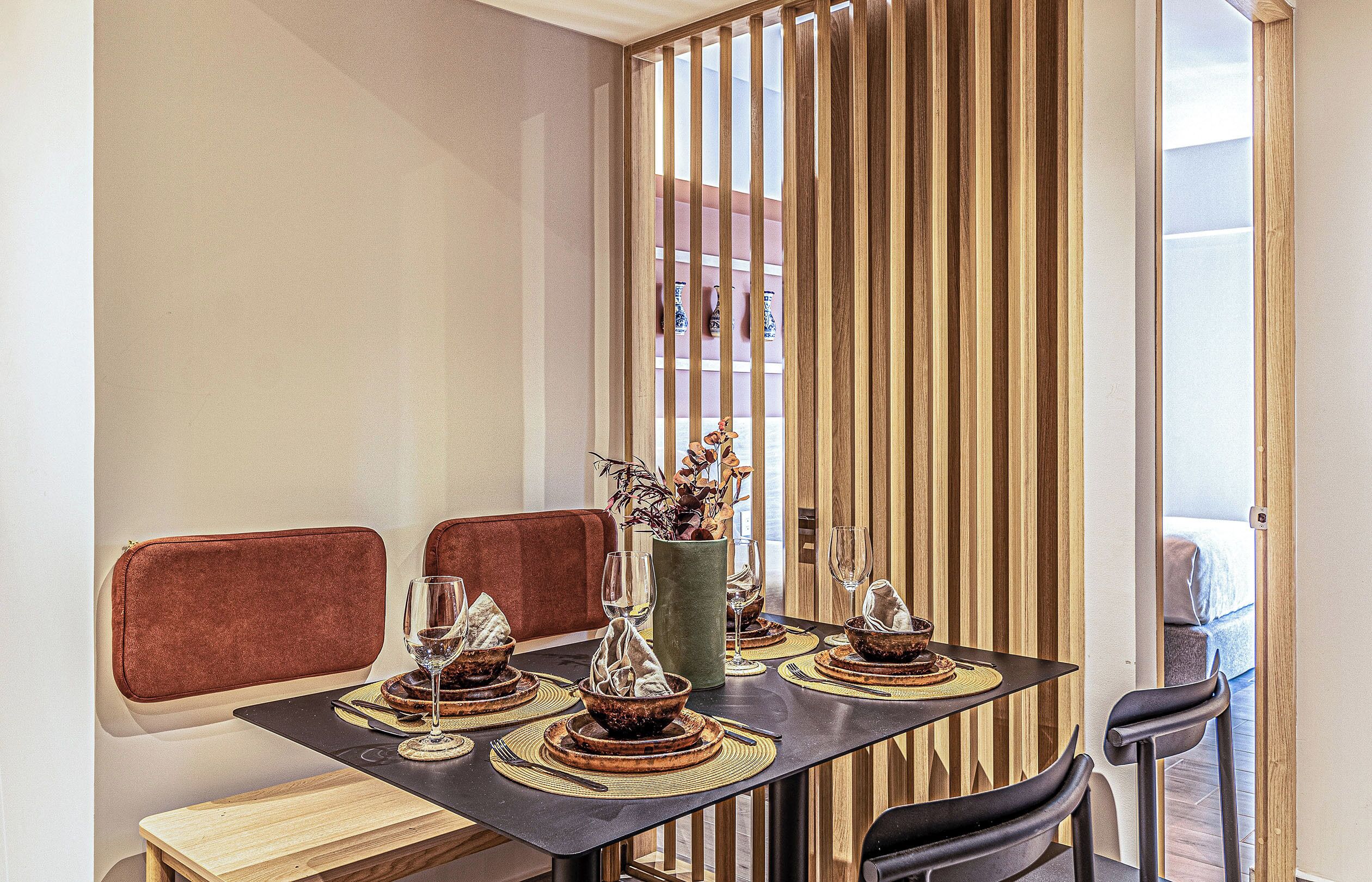 Un coin repas avec une table dressée pour quatre personnes, agrémenté de sets de table en fibres tressées, d’un vase avec des fleurs séchées et d’un bol décoratif.