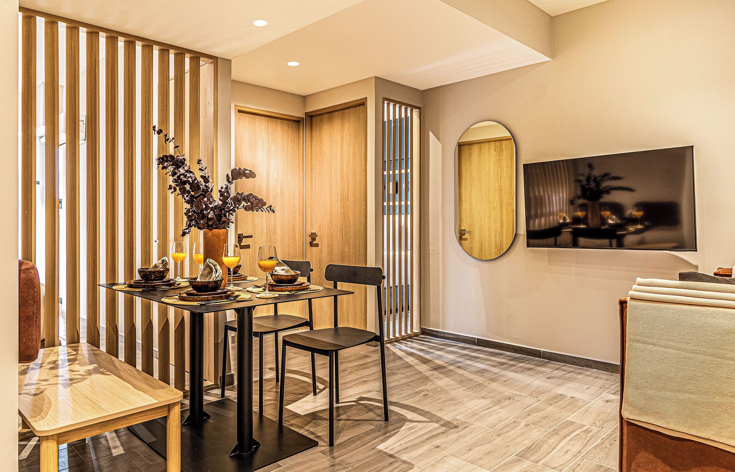 A modern dining area with a wooden partition, a round mirror, and a table set for two.