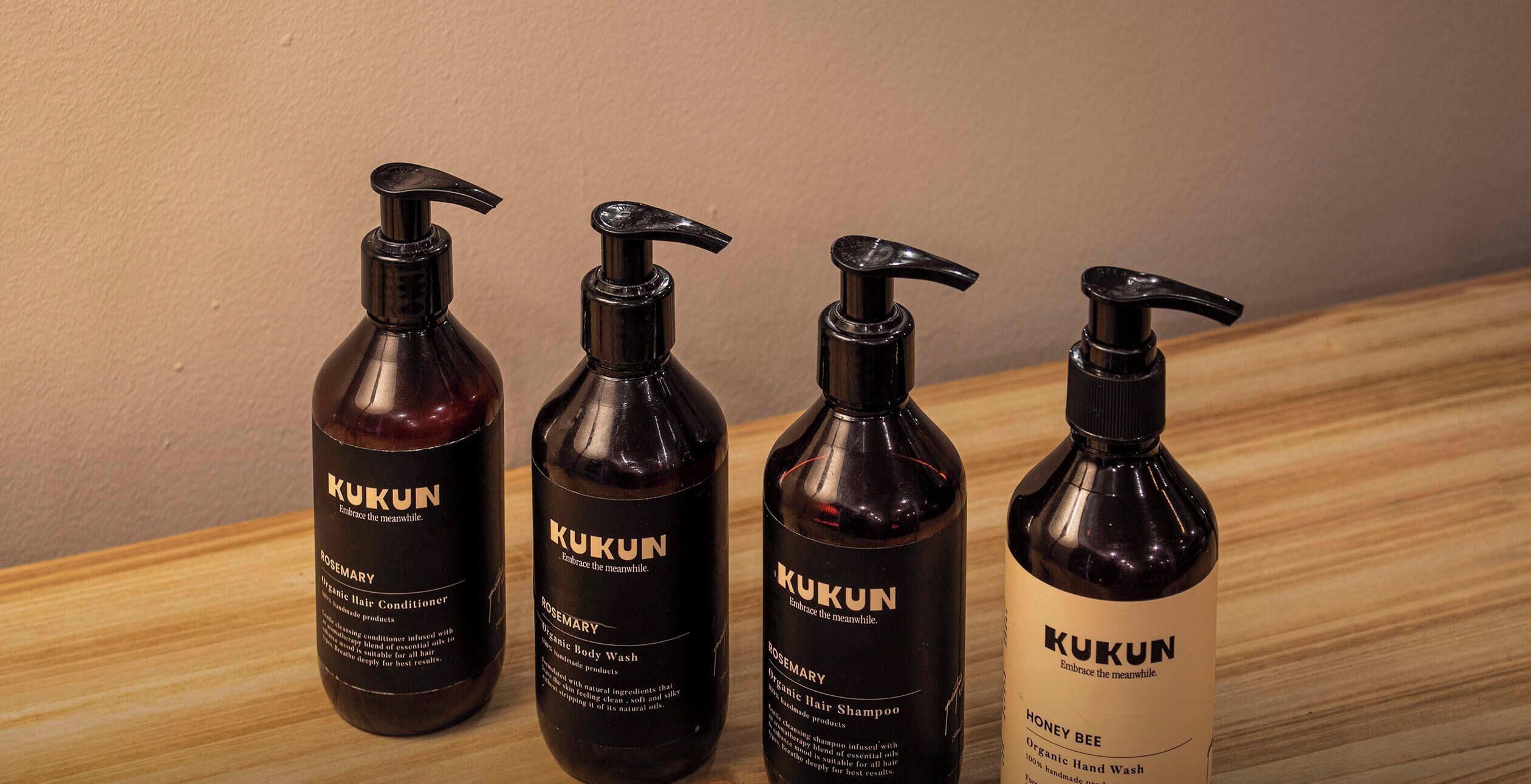 Cuatro botellas de productos capilares orgánicos Kukun sobre una superficie de madera.
