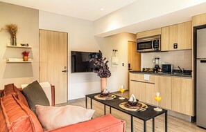 A modern kitchen with wooden cabinets, a microwave, and a coffee maker. There is a dining table with a vase and a glass of orange juice.