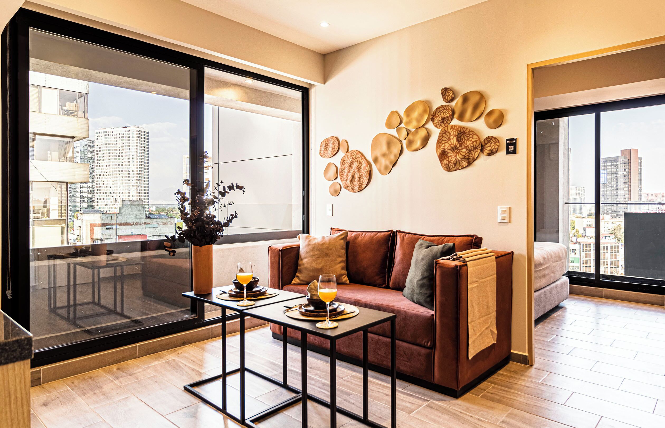 A modern living room with a sofa, a coffee table, and a large window offering a city view.