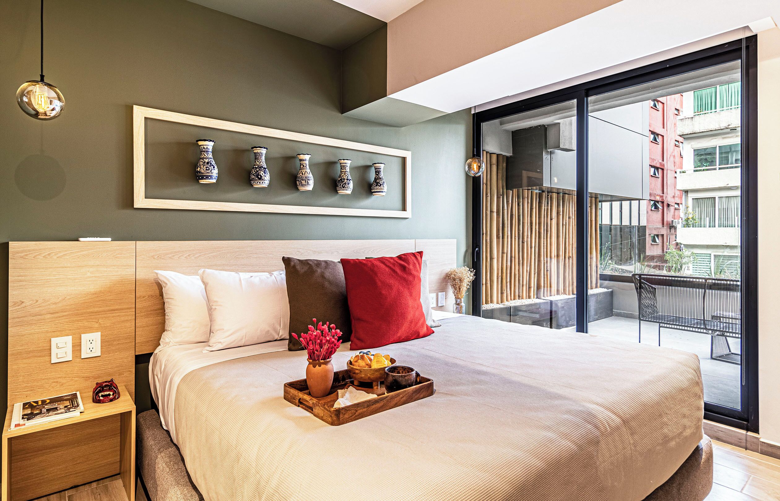 Habitación de hotel moderna con una cama grande, una mesita de noche, un arreglo de jarrones en la pared y un balcón con vista a la ciudad.