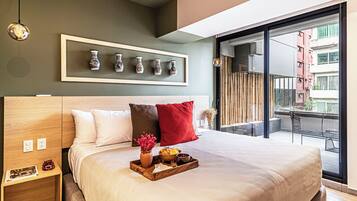Habitación de hotel moderna con una cama grande, una mesita de noche, un arreglo de jarrones en la pared y un balcón con vista a la ciudad.