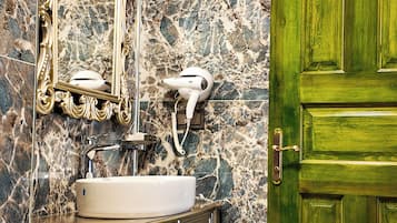 Un baño con pared de mármol, espejo con marco dorado, lavamanos y puerta verde.