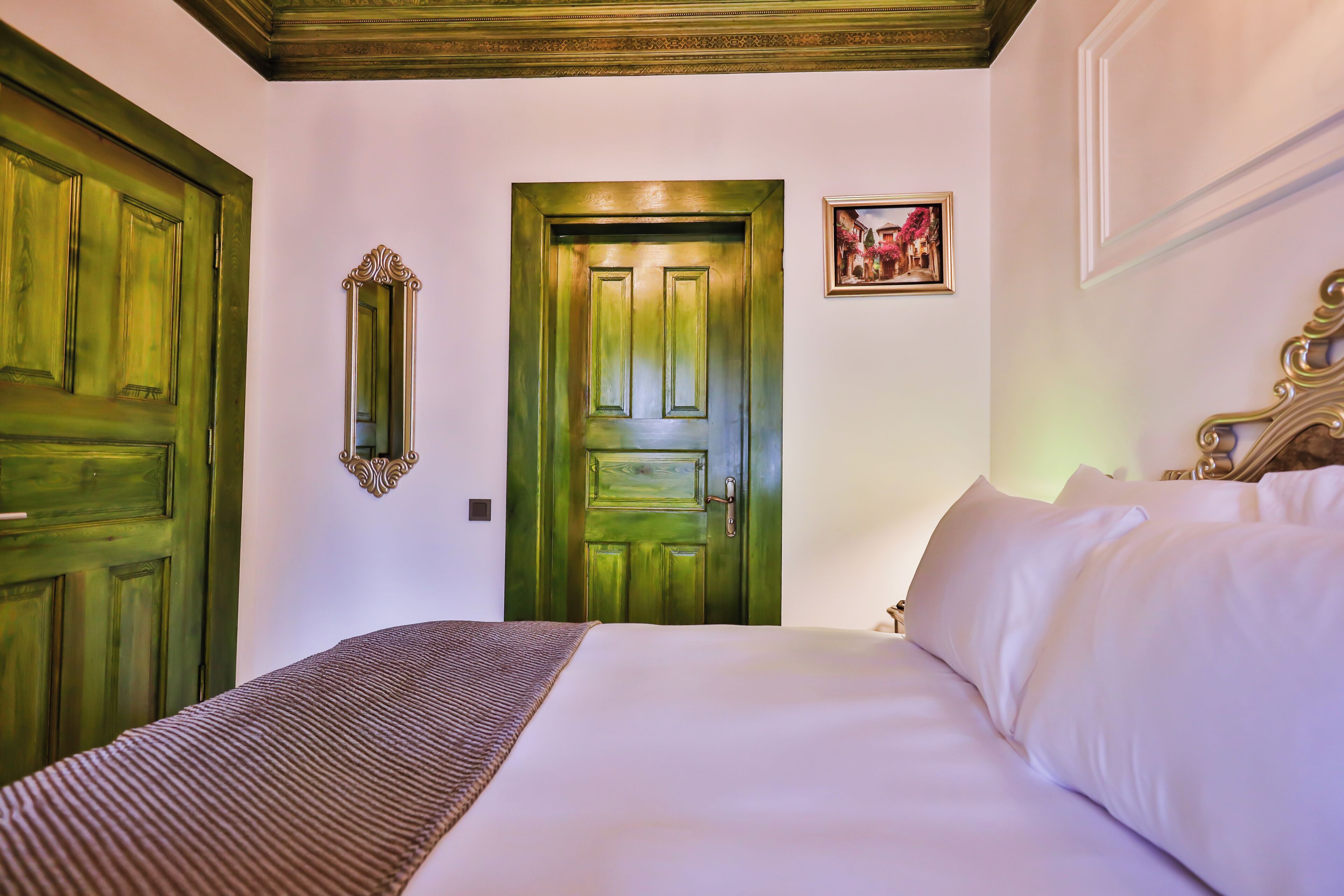 Habitación de hotel con una cama grande, una puerta verde, un espejo y un cuadro en la pared.
