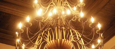 A chandelier with multiple light bulbs hanging from a central point, set against a ceiling with a geometric pattern.