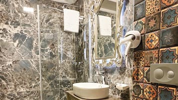 Un baño con piso de mármol, lavamanos, inodoro, ducha y un espejo decorativo.