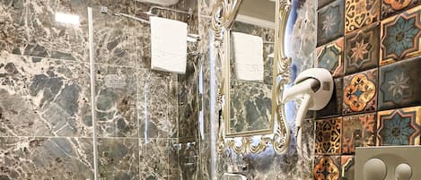 Un baño con piso de mármol, lavamanos, inodoro, ducha y un espejo decorativo.