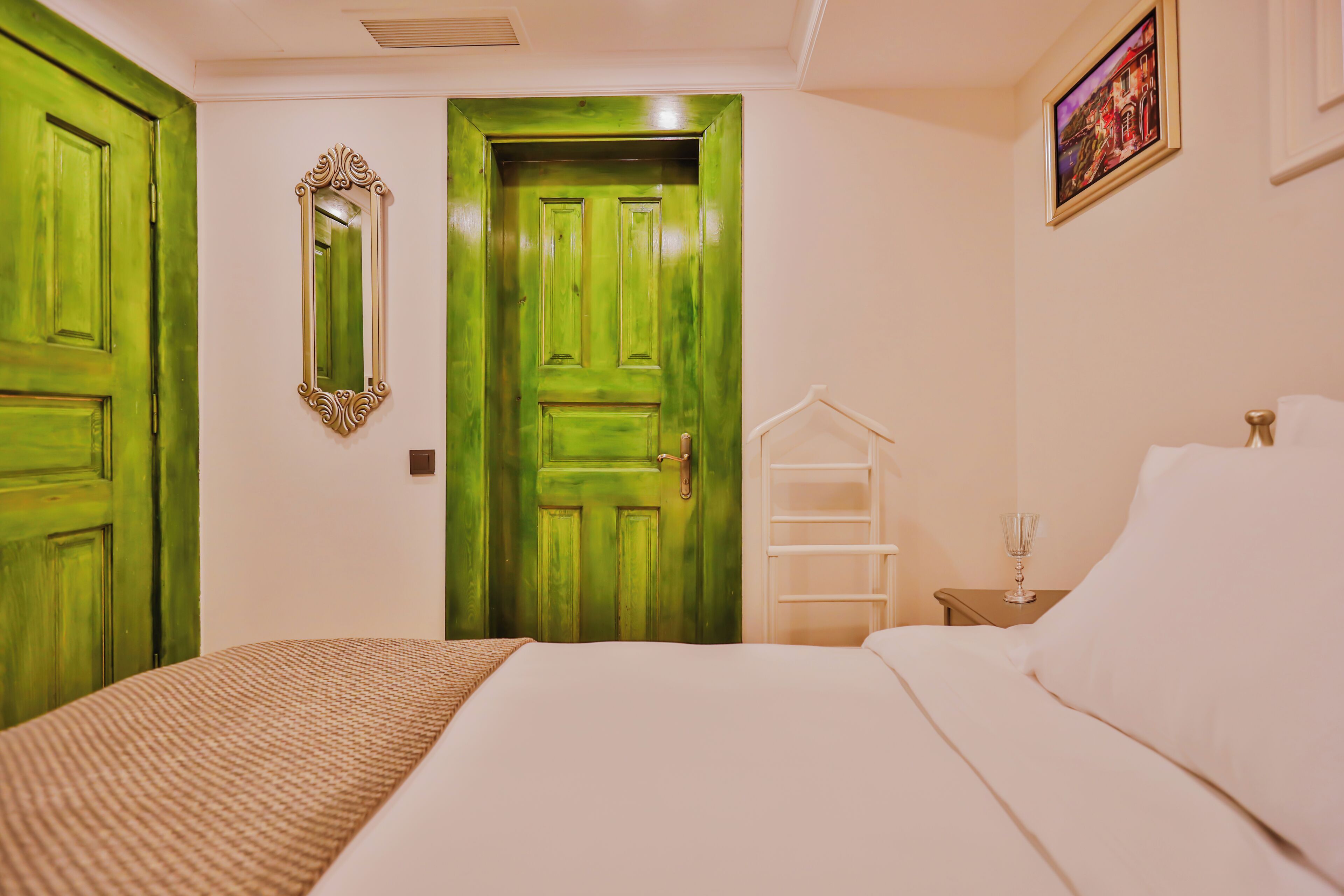 Quarto com uma cama, porta verde, espelho e um quadro na parede.
