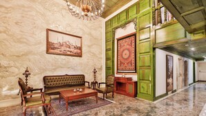 Un hall d’entrée avec un sol en marbre, un canapé, des fauteuils, une table basse, un lustre, un tableau encadré et un tapis à motifs.