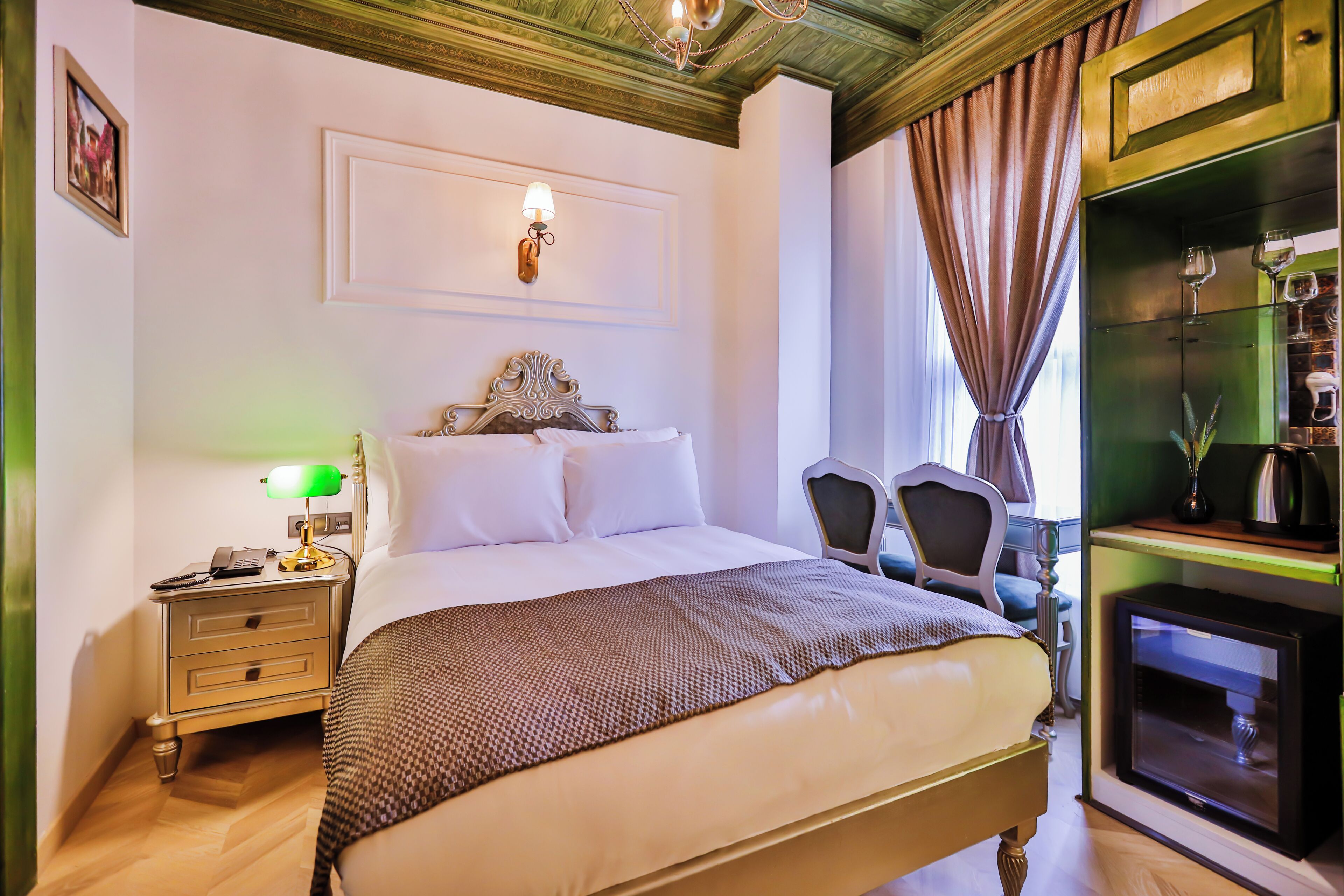 A hotel room with a bed, nightstand, lamp, chair, and a minibar.