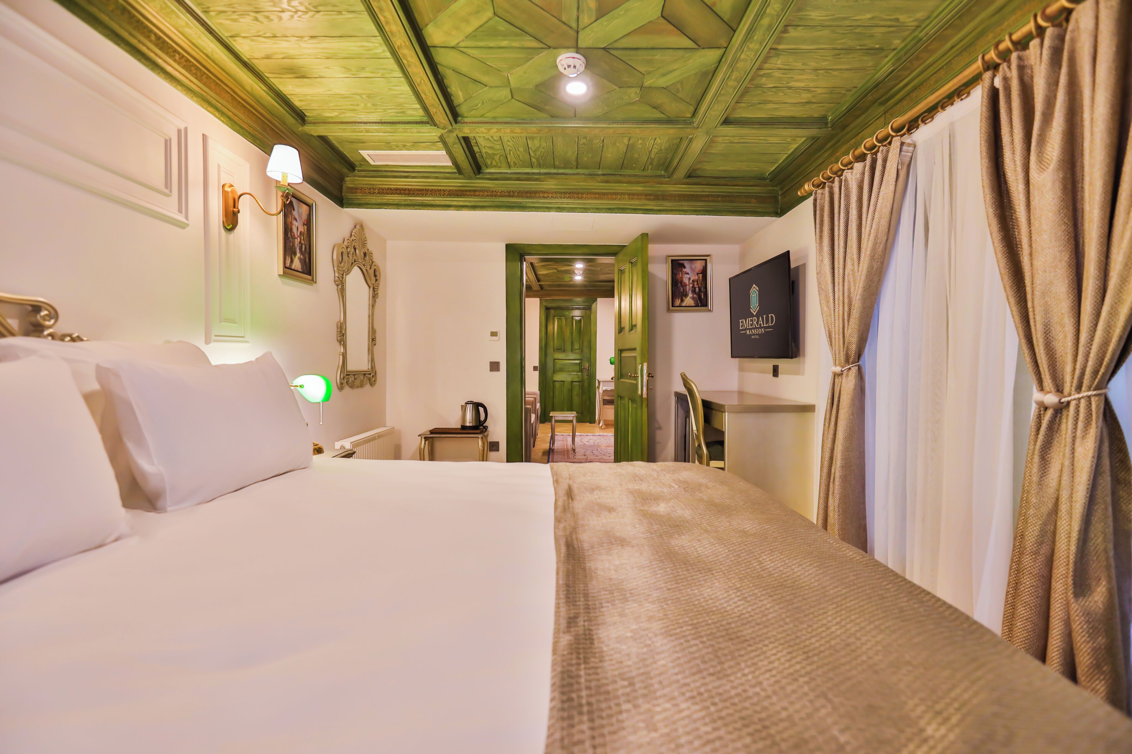 A hotel room with a large bed, a television, a green door, and a ceiling fan.