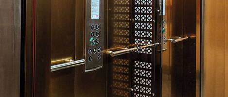 An elevator interior with metallic walls, a control panel with buttons, and a patterned door.