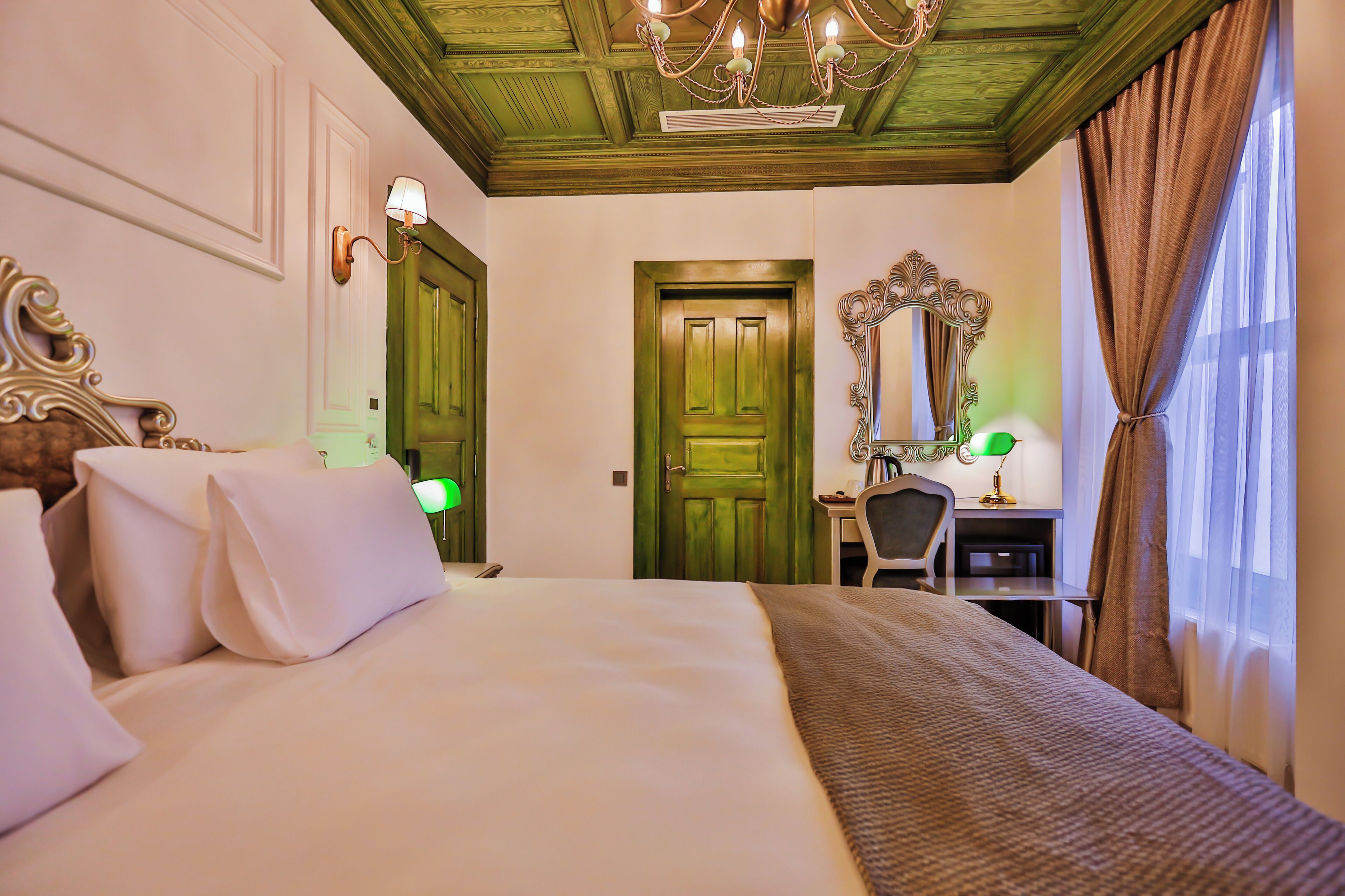 A hotel room with a large bed, a desk, a chair, a mirror, and a green door.