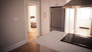 A modern kitchen with white cabinets, a stainless steel refrigerator, and a black stovetop. - Charming Meets Modern 2-bedroom Cottage (Morgan City)