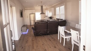 A modern kitchen with a central island, white cabinetry, and a dining area with a table and chairs. - Charming Meets Modern 2-bedroom Cottage (Morgan City)